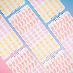 May include: Several sticker sheets with various emoji designs. The stickers feature pink hearts, yellow stars, and peach-colored thumbs-up emojis. The text "Rating Emojis" and a website address are printed on the sheets.