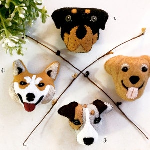 May include: Four felt dog head ornaments, each with a different breed. The ornaments are numbered 1 through 4. The dogs are a Rottweiler, a Golden Retriever, a Jack Russell Terrier, and a Corgi.