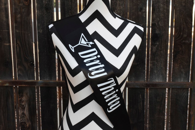 May include: Black satin sash with white text that reads "Dirty Thirty" and a martini glass icon.