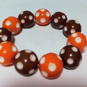 May include: A bracelet made of brown and orange beads with white polka dots.