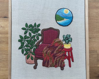 Nook 8: Maroon chair with umbrella plant, anthurium, and island coast art.