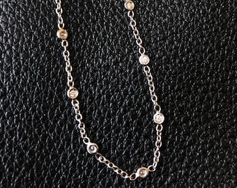 May include: A delicate silver bracelet with small, round, clear gemstones evenly spaced along the chain. The bracelet has a lobster clasp closure and a small extension chain. The background is a black, textured surface.