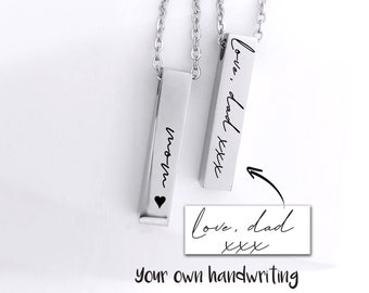 May include: Two silver-toned vertical bar necklaces with delicate chains. One bar is engraved with the word mom and a small heart symbol. The other bar features the engraved text love, dad xxx, matching the handwritten sample shown below it.