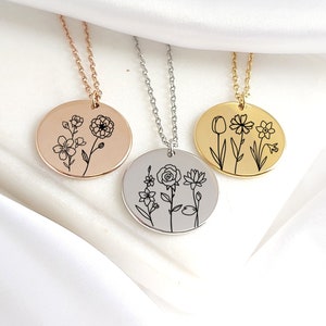 May include: Three round pendant necklaces with floral designs. The pendants are rose gold, silver, and gold, each with a delicate chain. The black line art depicts various flowers, including a marigold, rose, and tulip, on a white satin background.