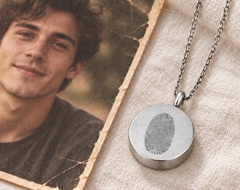 May include: A silver-toned circular pendant necklace featuring a detailed fingerprint engraving on its face. The pendant hangs from a delicate matching metal chain, positioned next to a square-shaped vintage-style photograph of a young person.