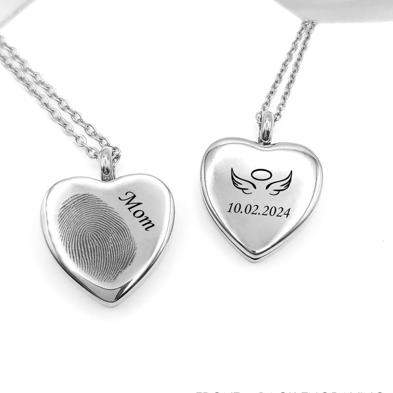 May include: Two silver-coloured heart-shaped pendants on delicate chains. The left pendant features an engraved fingerprint and the word Mom. The right pendant displays an engraved pair of angel wings with a halo above and the date 10.02.2024.