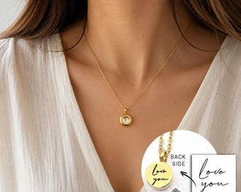 May include: A gold-toned necklace featuring a small circular pendant with a central clear stone. An inset shows the back of the pendant engraved with the cursive text 'love you' and a small pile of grey powder next to the metal charm.
