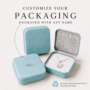 May include: Two light blue square metal tins with embossed floral borders. One tin is closed and engraved with the name Alex. The other tin is open, revealing a silver necklace with a round pendant featuring a small floral design inside.