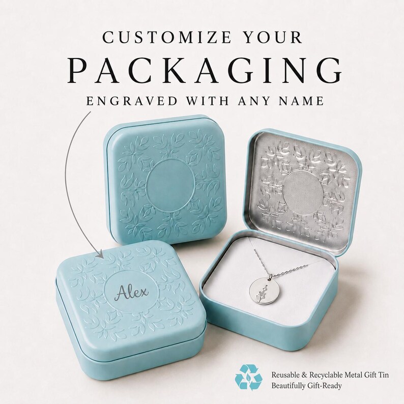 May include: Two light blue square metal tins with embossed floral borders. One tin is closed and engraved with the name Alex. The other tin is open, revealing a silver necklace with a round pendant featuring a small floral design inside.