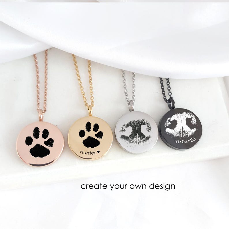 May include: Four circular pendant necklaces in rose gold, gold, silver, and black tones. Each pendant features a custom black engraved design, including animal paw prints and nose prints. One pendant includes the text Hunter and a heart, another 10.02.23.