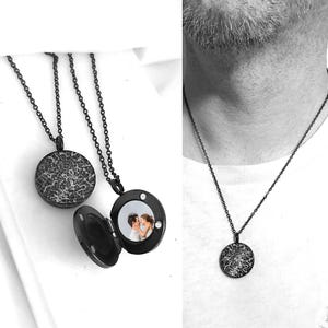 May include: A black circular locket necklace featuring a white star map design on the exterior. The locket opens to reveal a small circular photograph of two people inside. The pendant hangs from a matching black chain, shown worn around the neck.