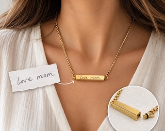May include: A gold-toned metal bar necklace featuring the engraved cursive text "love mom" on the front. The necklace includes a matching gold chain and a small inset image showing the bar unscrewed with a black rubber seal on the threaded end.