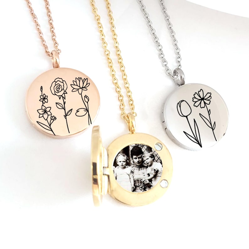 May include: Three round pendant necklaces with floral designs and a photo locket. One is rose gold with engraved flowers, another is gold with a photo inside, and the third is silver with a tulip and flower design. Each necklace has a delicate chain.