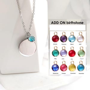 May include: A silver-toned necklace featuring a circular pendant and a small, round, blue birthstone charm. Beside it, a chart titled ADD ON birthstone displays twelve distinct colored crystal charms labeled by month from January to December.