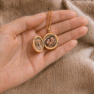 May include: A gold-toned circular locket necklace featuring a hinged design that opens to reveal two interior compartments. One side displays a photograph of a golden retriever puppy, while the other shows a couple with a golden retriever dog.