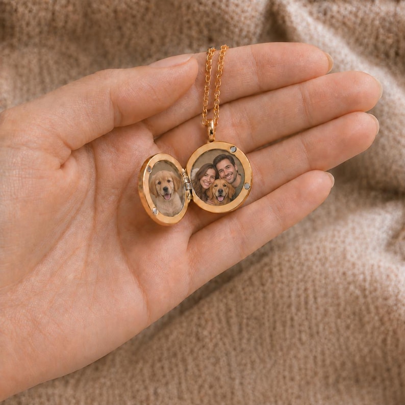 May include: A gold-toned circular locket necklace featuring a hinged design that opens to reveal two interior compartments. One side displays a photograph of a golden retriever puppy, while the other shows a couple with a golden retriever dog.