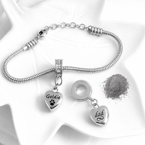 May include: A silver-toned snake chain bracelet with a lobster clasp and an adjustable extender chain. Two heart-shaped charms are included; one is engraved with the name Goldie and a paw print, and the other with the word dad and an infinity symbol.