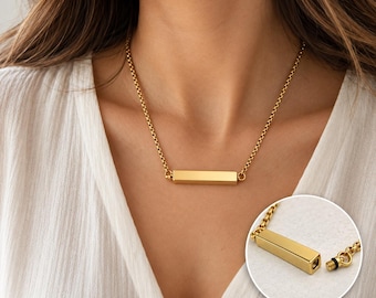 May include: A gold-toned necklace featuring a horizontal rectangular bar pendant suspended from a rounded link chain. The inset circular detail shows the bar pendant detached from the chain, revealing a threaded screw end and a small black rubber seal.