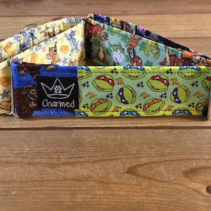Puede incluir: Un collar para perros con diseños de dibujos animados, incluyendo Tom y Jerry y las Tortugas Ninja. El collar tiene un anillo en D de metal y una etiqueta que dice "Charmed".