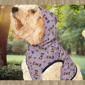 Könnte beinhalten: Ein helllila Hundepullover mit einem Regenbogenknochen- und Herzmuster. Der Pullover hat einen schwarzen Saum und eine Kapuze.