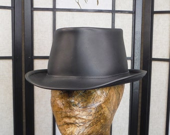 May include: A black leather fedora hat with a wide brim. The hat is sitting on a mannequin head.