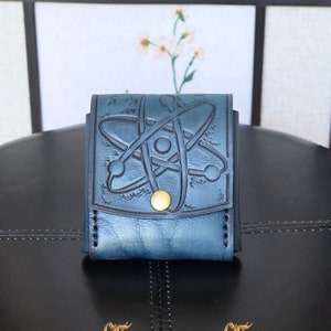 May include: A blue leather wallet with a tooled atom design. The wallet has a gold button closure and is sitting on a black surface.