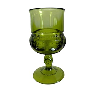 Puede incluir: Copa vintage verde con base redonda, tallo decorativo y sección media bulbosa con detalles en relieve. La parte superior tiene una forma cilíndrica simple. El vidrio tiene un ligero tinte oliva.