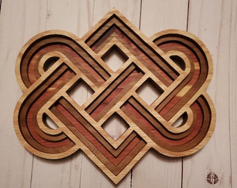 May include: A multi-layered wooden wall art piece featuring an intricate, symmetrical Celtic knot design. The object is constructed from stacked wood segments in varying shades of light tan, reddish-brown, and dark brown, creating depth.