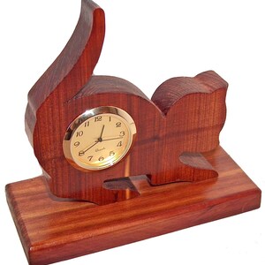 May include: A wooden cat-shaped clock with a gold-colored face and black hands. The clock is sitting on a wooden base.