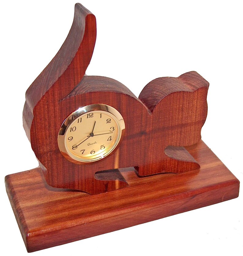 May include: A wooden cat-shaped clock with a gold-colored face and black hands. The clock is sitting on a wooden base.