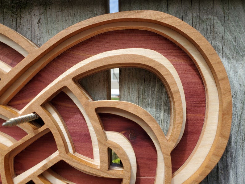 May include: A multi-layered wooden wall art piece featuring intricate, interlocking curved shapes. The design consists of alternating layers of light-toned wood and deep reddish-brown wood, creating a dimensional, stacked effect with visible depth.