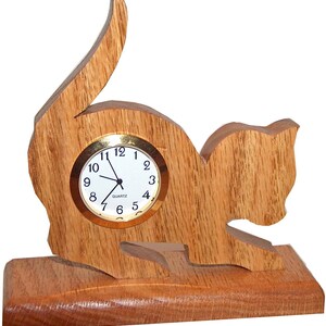 May include: A wooden cat-shaped clock with a round, white face and gold-colored hands. The clock is sitting on a wooden base.