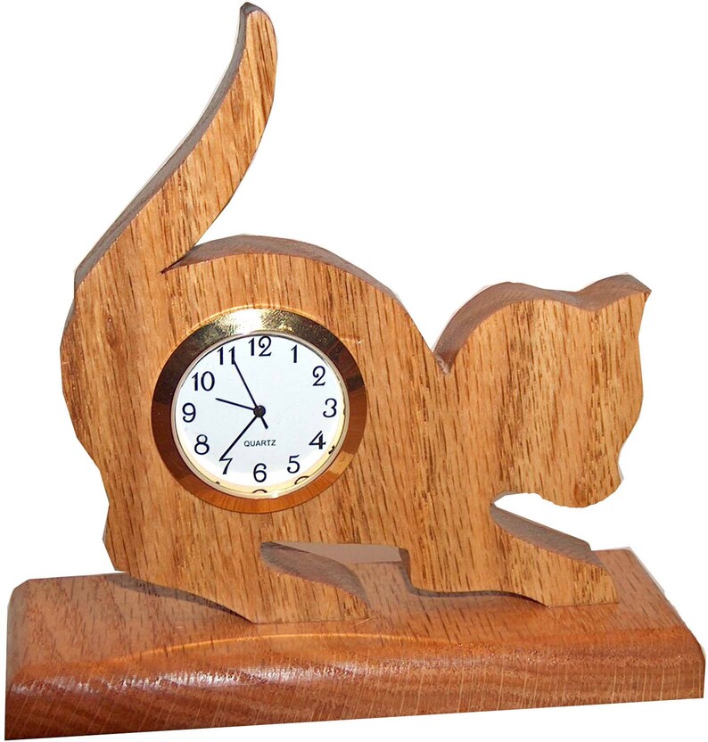 May include: A wooden cat-shaped clock with a round, white face and gold-colored hands. The clock is sitting on a wooden base.