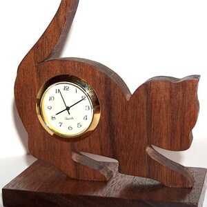 May include: A wooden cat-shaped clock with a gold-rimmed face and black hands. The clock is sitting on a wooden base.