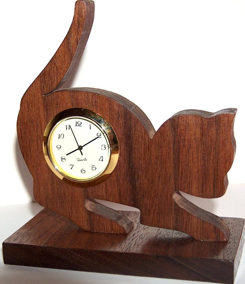 May include: A wooden cat-shaped clock with a gold-rimmed face and black hands. The clock is sitting on a wooden base.