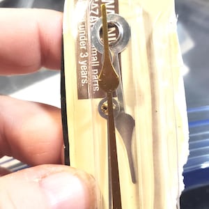 May include: Clock hands set, featuring a gold-tone hour hand and a silver-tone minute hand. The hour hand has a decorative teardrop shape. The packaging includes a warning about small parts.