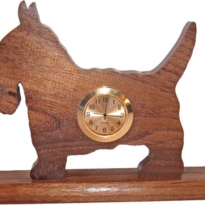 May include: A wooden clock shaped like a Scottish Terrier dog. The clock has a gold face with black numbers and hands. The dog is standing on a wooden base.