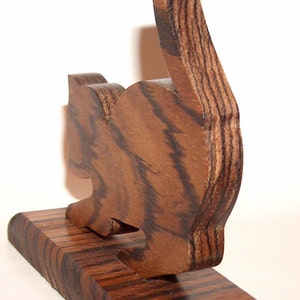 May include: A wooden cat figurine with a brown and black striped pattern. The cat is standing on a wooden base.