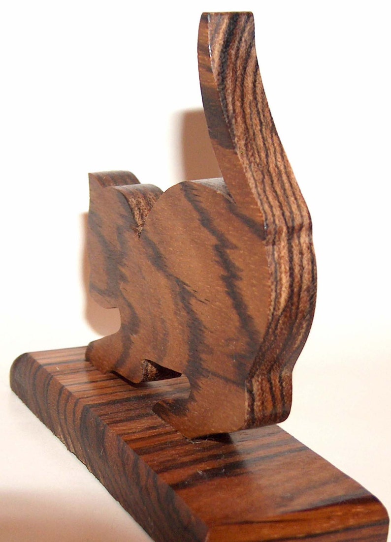 May include: A wooden cat figurine with a brown and black striped pattern. The cat is standing on a wooden base.