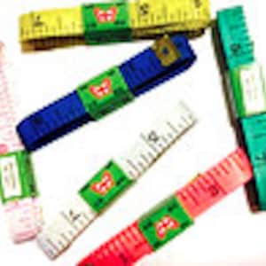 May include: Assortment of colorful measuring tapes in various colors, including pink, white, red, green, blue, and yellow. Each tape is rolled up and labeled with a green sticker. The tapes are designed for measuring in inches and centimeters.