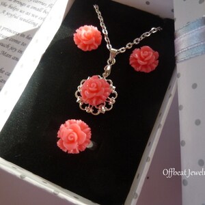 May include: A coral-colored jewelry set featuring a rose design, presented in a polka-dot gift box. The set includes a necklace, earrings, and a ring. The necklace pendant is surrounded by a silver filigree. The text "Offbeat Jewelry" is visible on the box.