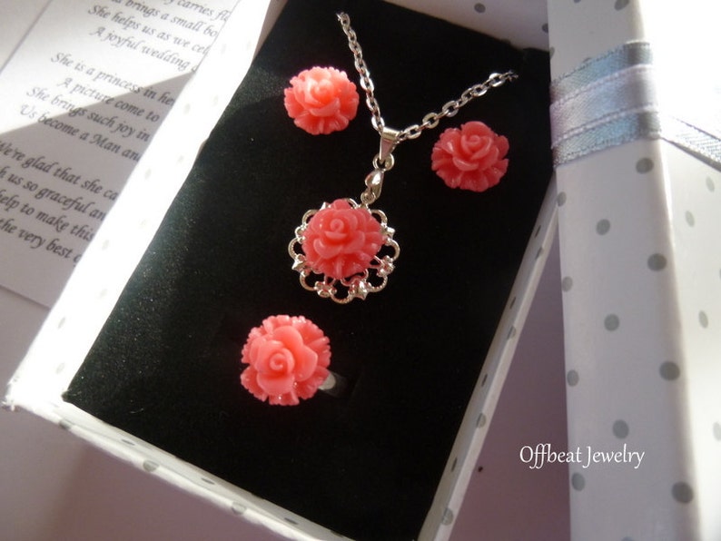 May include: A coral-colored jewelry set featuring a rose design, presented in a polka-dot gift box. The set includes a necklace, earrings, and a ring. The necklace pendant is surrounded by a silver filigree. The text "Offbeat Jewelry" is visible on the box.
