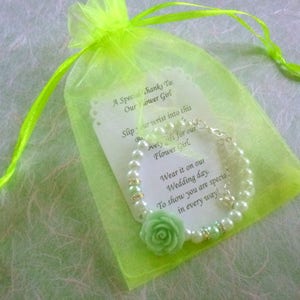 Op de afbeelding: Een groene en witte parel armband met een groene bloemenbedel wordt geleverd in een groene organza tas. De tas heeft een kaartje met de tekst "Een speciale dank aan onze bruidsmeisje. Schuif je pols in dit mooie cadeau voor onze bruidsmeisje. Draag het op onze trouwdag. Om te laten zien dat je op alle manieren speciaal bent!"