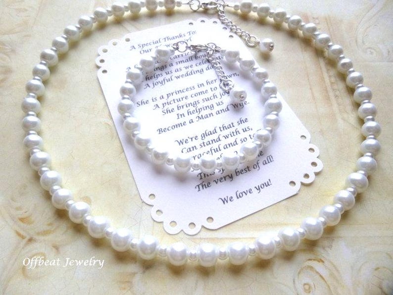 May include: A white pearl necklace and matching bracelet set. The jewelry is displayed on a decorative card with text. The necklace and bracelet are made of round, white pearls and silver-toned clasps.