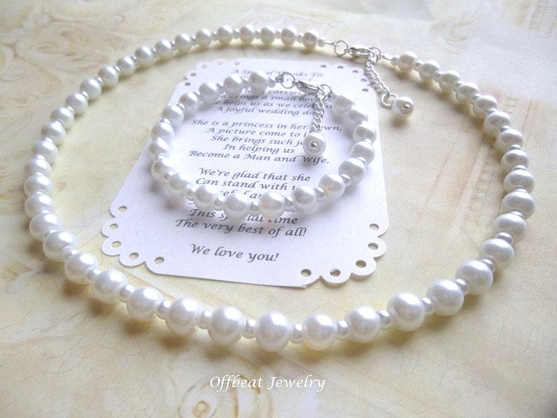 May include: A white pearl necklace and matching bracelet set. The jewelry is displayed on a white card with text. The necklace and bracelet are made of round, white pearls and have silver-colored clasps.
