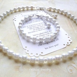 May include: A white pearl necklace and matching bracelet set. The jewelry is displayed on a white card with a scalloped edge and text. The set is likely for a wedding or special occasion. The jewelry is from Offbeat Jewelry.