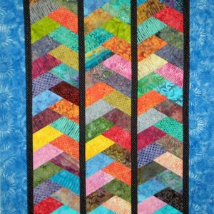 May include: A quilt with three vertical panels of colorful fabric arranged in a chevron pattern. Each panel is bordered by black fabric with white polka dots. The quilt is framed by a blue fabric with a white pattern.