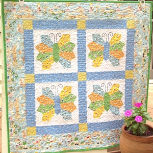 May include: A blue and white quilt with a yellow and green butterfly design. The quilt is framed with a green border and a blue and white border. The quilt is hanging on a white wall.