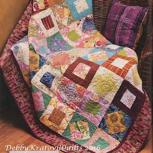 May include: A colorful quilt with a patchwork design featuring squares and diamonds. The quilt is made with a variety of fabrics in shades of pink, purple, green, orange, and brown. The quilt is displayed on a wicker chair with a purple pillow. The text "Debby Kratovil Quilts 2016" is visible in the lower right corner of the image.