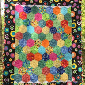Puede incluir: Una colcha colorida con un patrón de panal de abeja hecha de tela con diferentes diseños de lunares. La colcha está bordeada con una tela negra con lunares coloridos. La colcha está firmada "Debby Kratovil Quilts 2018".